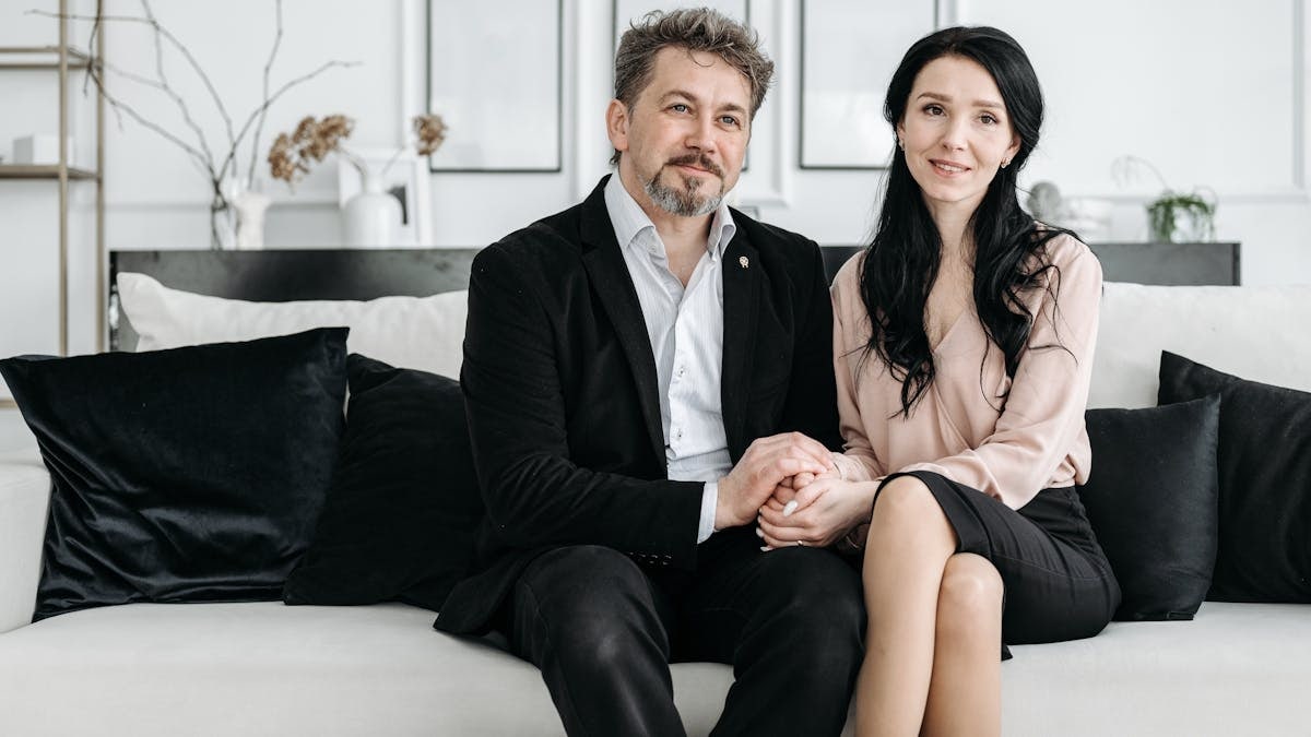 Smiling couple holding hands while sitting on a modern sofa in a stylish living room.